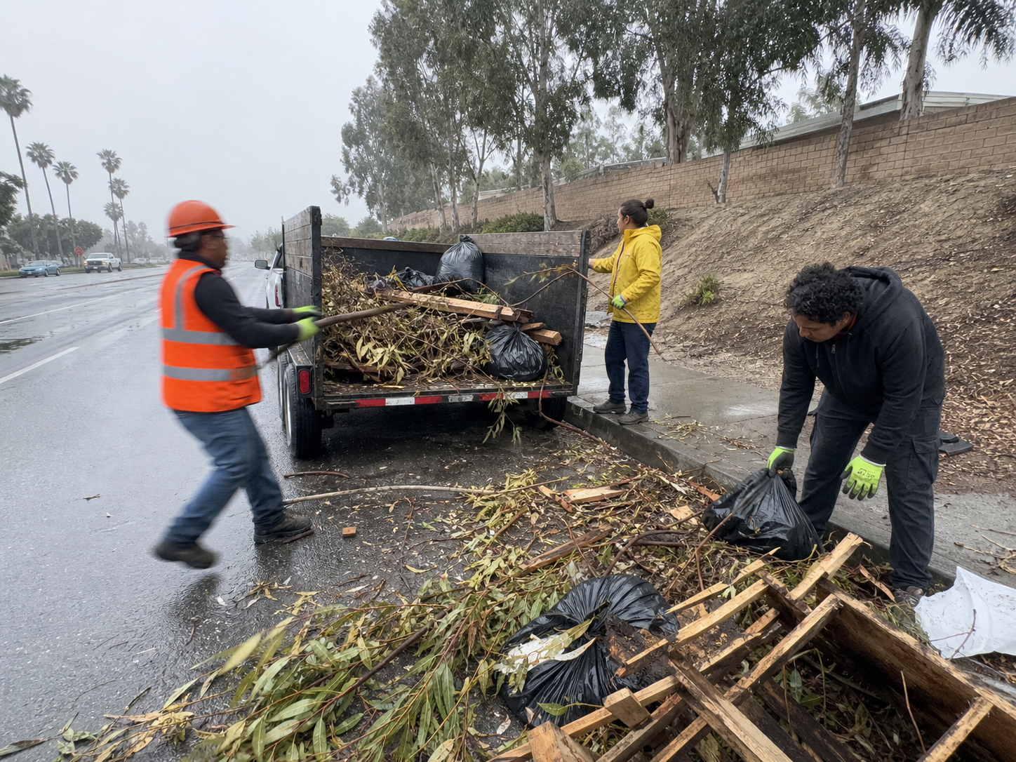 High-visibility cleanup crew documenting a route beside a trailer and bagged debris